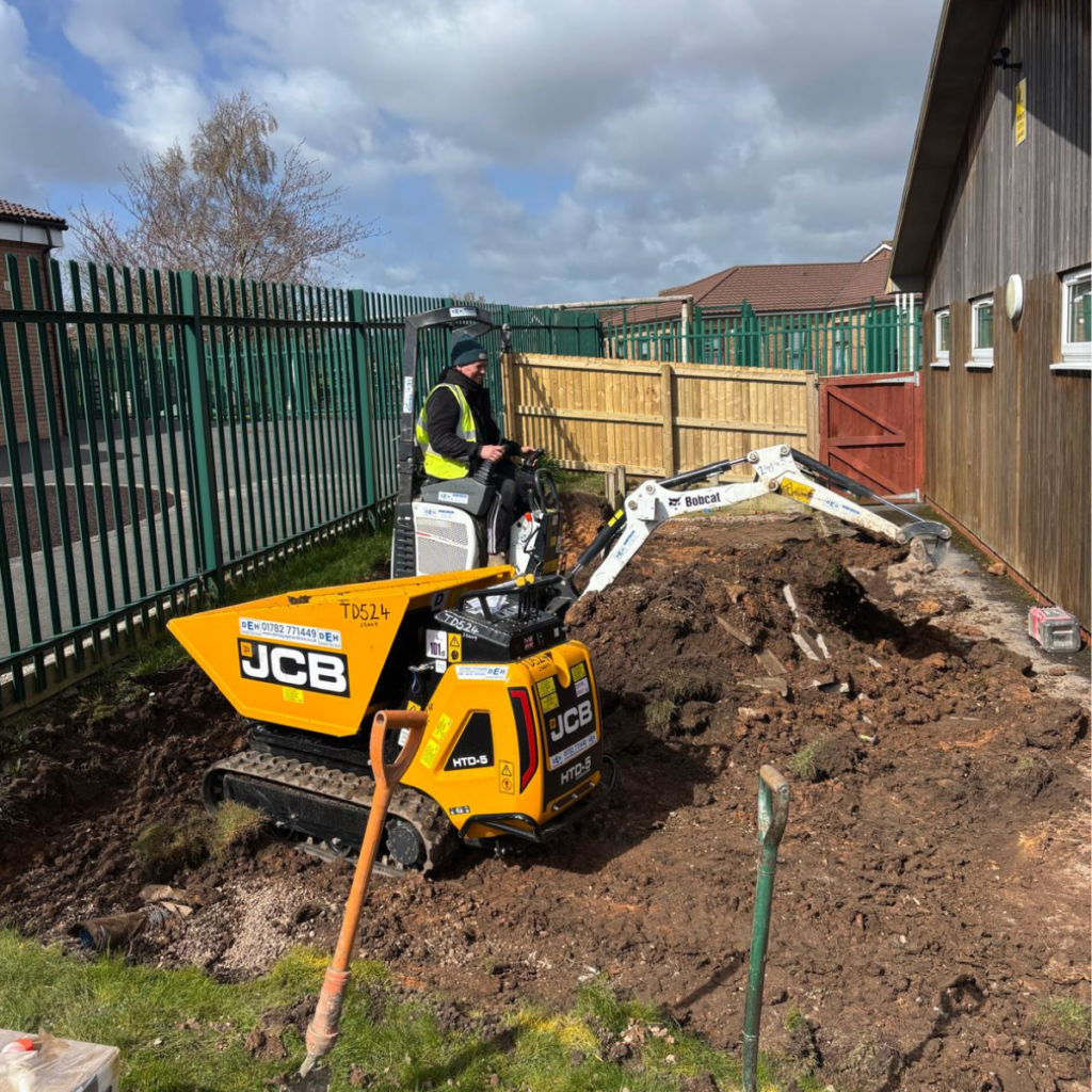 A groundworker loading a tracked wheelbarrow with a mini-digger