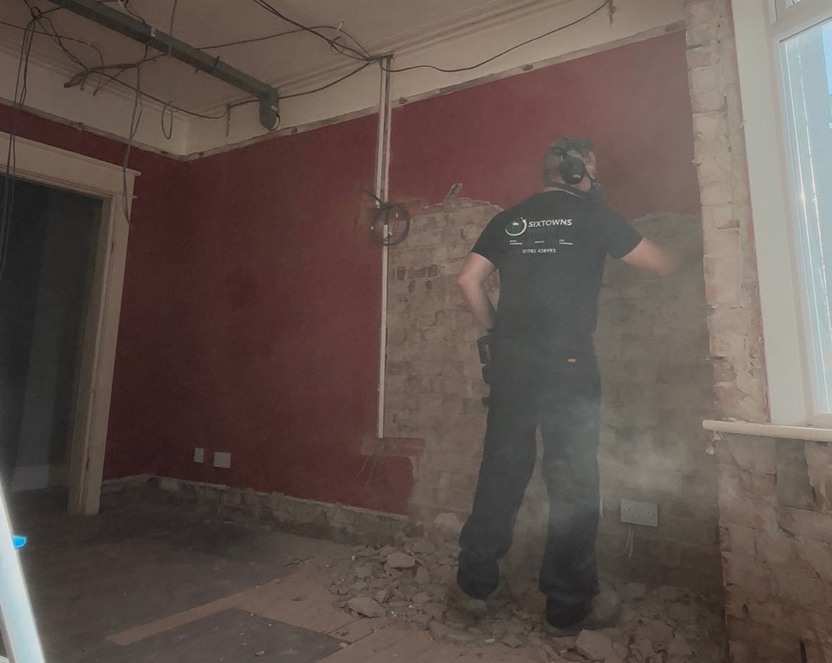 A worker removing plaster from a wall in a HMO
